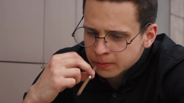 Человек в круглых очках курит сигареты вблизи — стоковое видео