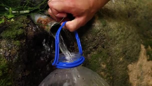 Человек черпает воду из источника в бутылку — стоковое видео