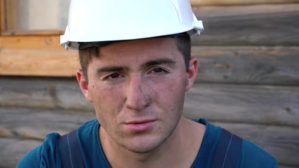 Un buen trabajador de la construcción con un sombrero duro mira a la cámara y sonríe — Vídeos de Stock