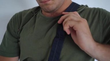 Bir adam tişörtün üstüne perçin ve tulum giyer.