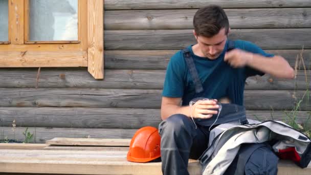 Arbeiter wischt nach Feierabend seine Brille vom Staub, während er auf den Brettern sitzt — Stockvideo