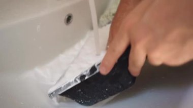 Bir adam lavaboda boya kovasını yıkıyor.