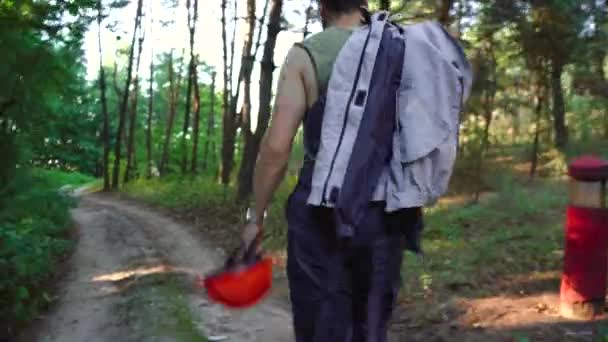 Bouwvakker loopt door het bos met zijn helm in zijn hand — Stockvideo