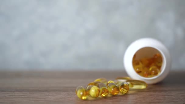 Tabletki oleju rybnego są na drewnianym stole. Jasnożółte błyszczące tabletki Omega 3. — Wideo stockowe