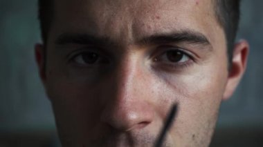 Evde oturan adam gözlük takıyor ve kameraya bakıyor.