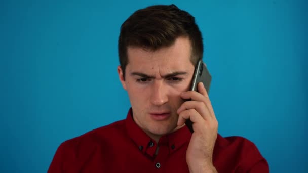 Man in a red shirt swears on the phone on a blue background — Stock Video