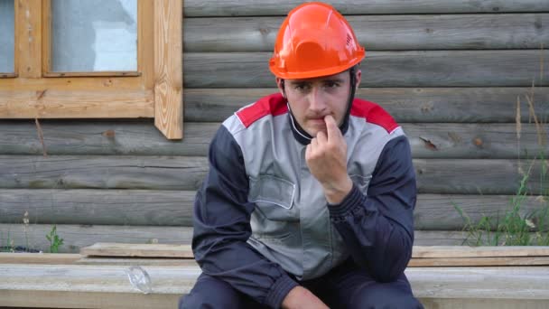 Mannelijke bouwvakker zit op planken en bijt zijn nagels — Stockvideo