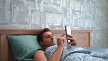 Adam yatakta yatarken telefon kullanıyor.