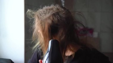 Kız saçını saç kurutma makinesiyle kurutuyor.