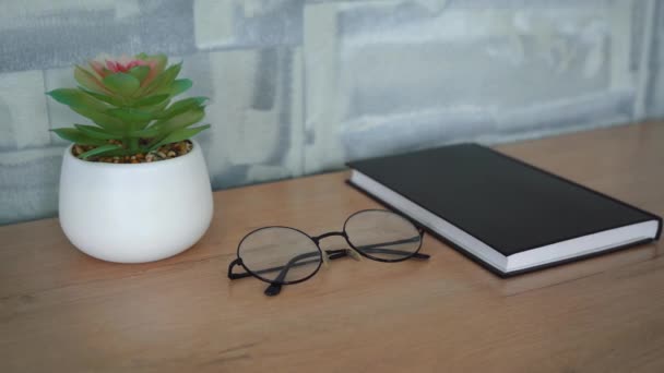 Mesa de madeira em que se encontra um caderno, óculos e uma flor — Vídeo de Stock