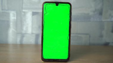 Yeşil ekranlı telefon ahşap bir masada dikiliyor..
