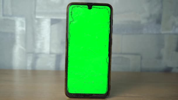 Teléfono con una pantalla verde de pie sobre una mesa de madera. — Vídeos de Stock