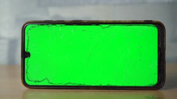 En telefon med grønn skjerm står horisontalt på et trebord – stockvideo