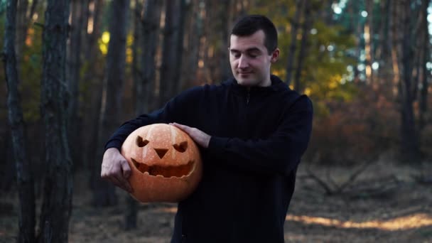 Un hombre sostiene una calabaza en su mano mientras está de pie en el bosque — Vídeos de Stock