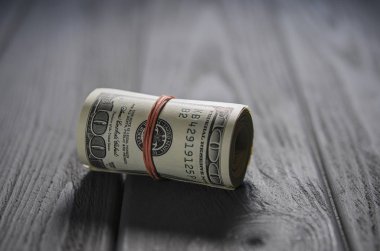 Kırmızı bir yüz dolarlık banknot kalın bir rulo bağlı lastik bant gri ahşap masa üzerinde yatıyor