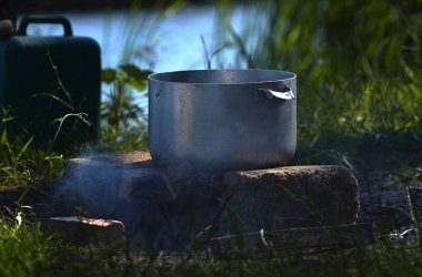 Bir piknik Nehri yakınında, büyük bir metal tava hangi balık çorbası duman ve yeşil çim arka planı hazırlanmıştır taşları üzerine duruyor..