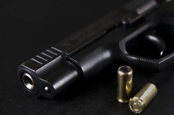 Черная пушка лежит на черном фоне рядом с патронами.
