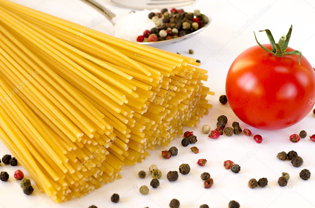 Ingredients for Italian cooking: Spaghetti lie on a white background, along with cherry tomatoes, a spoon in which lies the pepper and the fork