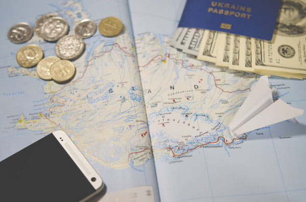 The plane, smartphone, biometric passport, dollars, coins and credit cards lie on a map