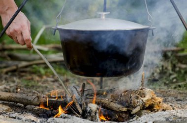 Bir adamın elini ateşin üzerinde duran siyah bir pan altında yangın kindles.