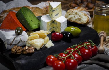 Camembert, brie, parmesan peyniri, domates, zeytin, sarımsak, fındık ve bal ahşap bir masa üzerinde yanındaki karanlık bir gemide fesleğen ve kırmızı biber peynir yalan ile yeşil peynir