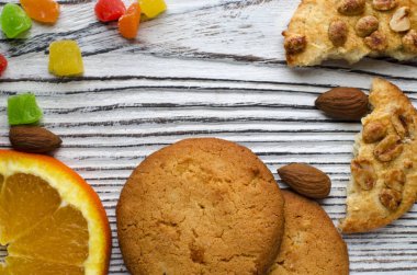 Renkli şekerlenmiş meyve ve sulu turuncu tahta bir masanın üzerinde yatan bir dilim ile yuvarlak portakal bisküvi. Portre