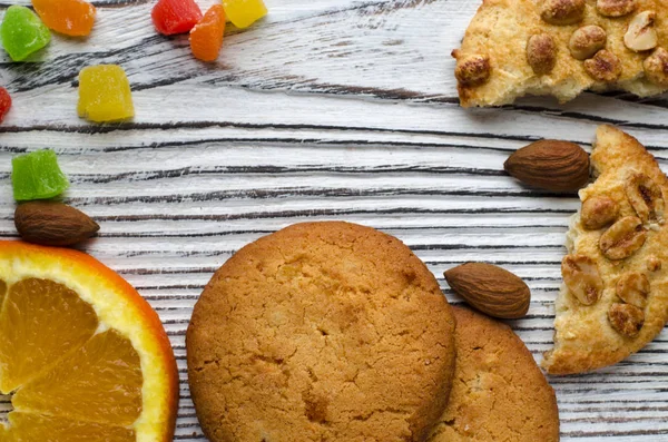 Renkli şekerlenmiş meyve ve sulu turuncu tahta bir masanın üzerinde yatan bir dilim ile yuvarlak portakal bisküvi. Portre