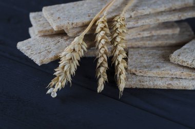 Hava diyet somun yalan buğday kulakları yanındaki karanlık bir arka plan üzerinde koyu ahşap bir masa üzerine. Ekmek kopya alan arka plan ağaç sınırında. Kahverengi ve beyaz tam tahıl somun natürmort kompozisyon buğday kulakları ile dağılmış. Ekmek pasta ve gro