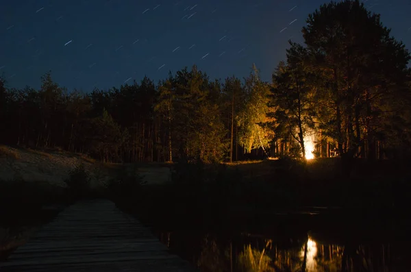 Gece ormandaki şenlik ateşi. Gece görüş-in geleneksel tarzı ahşap köprü Nehri üzerinden. Ormana doğru giden Nehri üzerinde ahşap köprü.