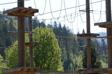 Ahşap sütunlar ve Karpatlar yeşil orman arka plan üzerinde bir halat parkının asılı halatlar