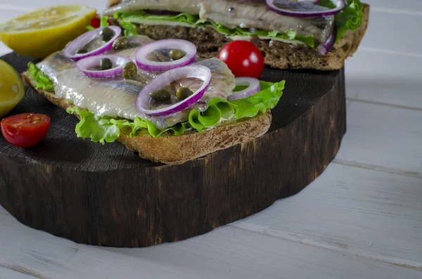 Sandwich mit gesalzenem Hering, Butter und roten Zwiebeln auf einem alten rustikalen Schneidebrett. Selektiver Fokus — Stockfoto