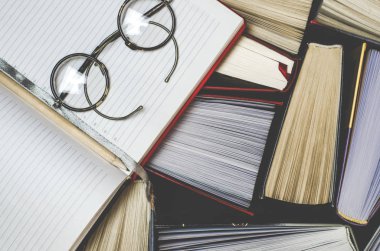 Çok çok renkli kalın açık kitap karanlık bir arka plan üzerinde durmak. Yuvarlak gözlük ve açık bir defter bir kalem ile eski kitaplardır.