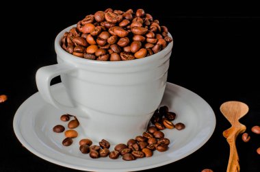 Beyaz fincan kahve çekirdekleri tam bir tahta kaşık yanında siyah bir arka plan üzerinde beyaz bir daire üzerinde duruyor