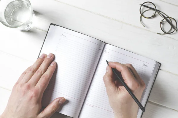 L'homme écrit des notes sur le carnet de notes sur une table en bois dans son bureau à domicile — Photo