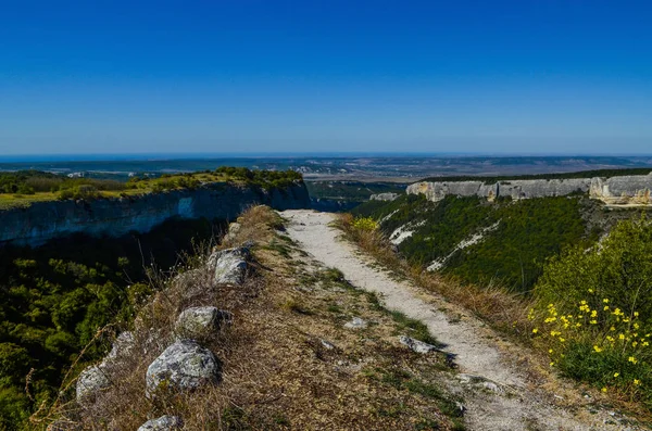 Trilha de montanha de pedra leva ao precipício contra um pano de fundo de céu azul — Fotografia de Stock