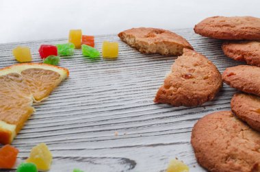 Renkli şekerlenmiş meyve ve sulu turuncu ahşap bir masa kış orman arka planı üzerinde yatan bir dilim ile yuvarlak portakal bisküvi