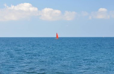 Mavi bir arka planda, mavi deniz boyunca yüzen kırmızı yelkenli bir tekne.