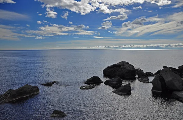거대한 검은 돌은 흰 구름과 푸른 하늘에 푸른 바다에 누워. — 스톡 사진