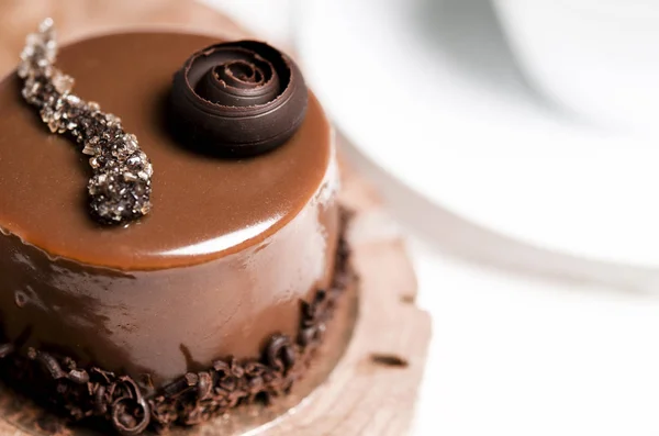 Een heerlijke chocolate cake met chocoladestukjes ligt op een houten tribune naast een witte beker, die op een witte tafel staat — Stockfoto