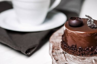 Bir ahşap stand yanında beyaz bir masada duran beyaz bir fincan lezzetli çikolatalı pasta çikolata parçaları ile yatıyor