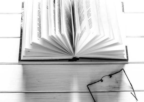 Open book ready to read lies on a white wood table next to the old round glasses. closeup