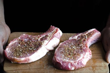 Elleri üzerinde baharat serpiştirilmiş ve pişirilmeye hazır iki domuz eti olan bir tahta tutuyor.
