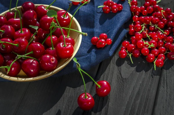 Cereza roja y grosellas se encuentran sobre un fondo de madera negra — Foto de Stock