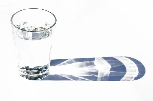 Water glass with strong shadows on white background — Stock Photo, Image