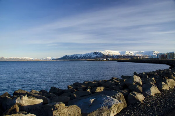 Skandinava táj. Az a kő töltés Reykjavik a háttérben a hegycsúcsok borított hó — Stock Fotó