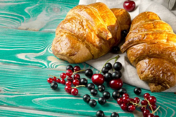 新鲜的红润羊角面包和浆果躺在一张木桌上,旁边是新鲜的黑醋栗浆果、红醋栗、樱桃 — 图库照片