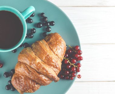 Taze siyah frenk üzümü çilek, kırmızı kuş üzümü yanında ahşap bir masa üzerinde çilek ile taze kirli kruvasanlar