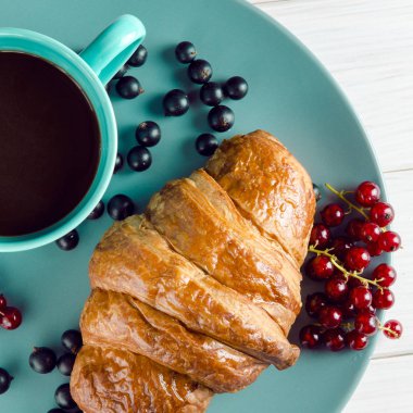 Taze siyah frenk üzümü çilek, kırmızı kuş üzümü yanında ahşap bir masa üzerinde çilek ile taze kirli kruvasanlar