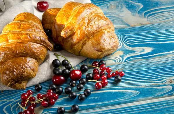 Verse, Ruddy croissants met bessen liggen op een houten tafel naast verse zwarte bessen, rode aalbessen, kersen — Stockfoto