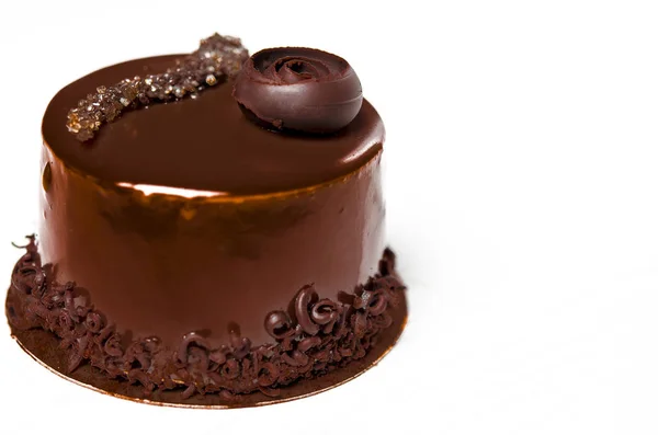 Un delicioso pastel de chocolate con trozos de chocolate se encuentra en un soporte de madera junto a una taza blanca, que se encuentra en una mesa blanca —  Fotos de Stock